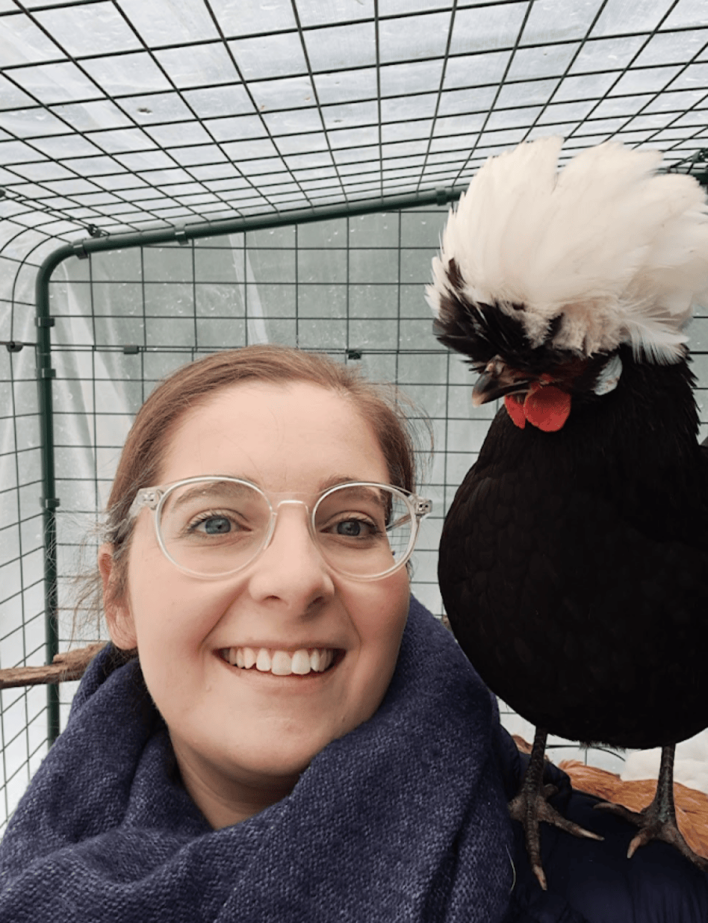 A woman smiling at the camera with a chicken on her shoulder